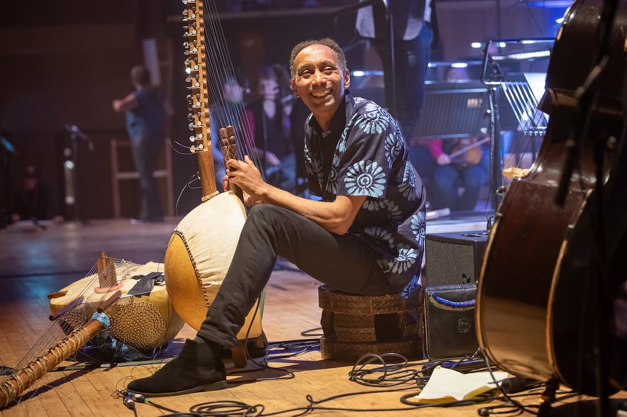 A smiling man looks at the camera as he plays the kora.