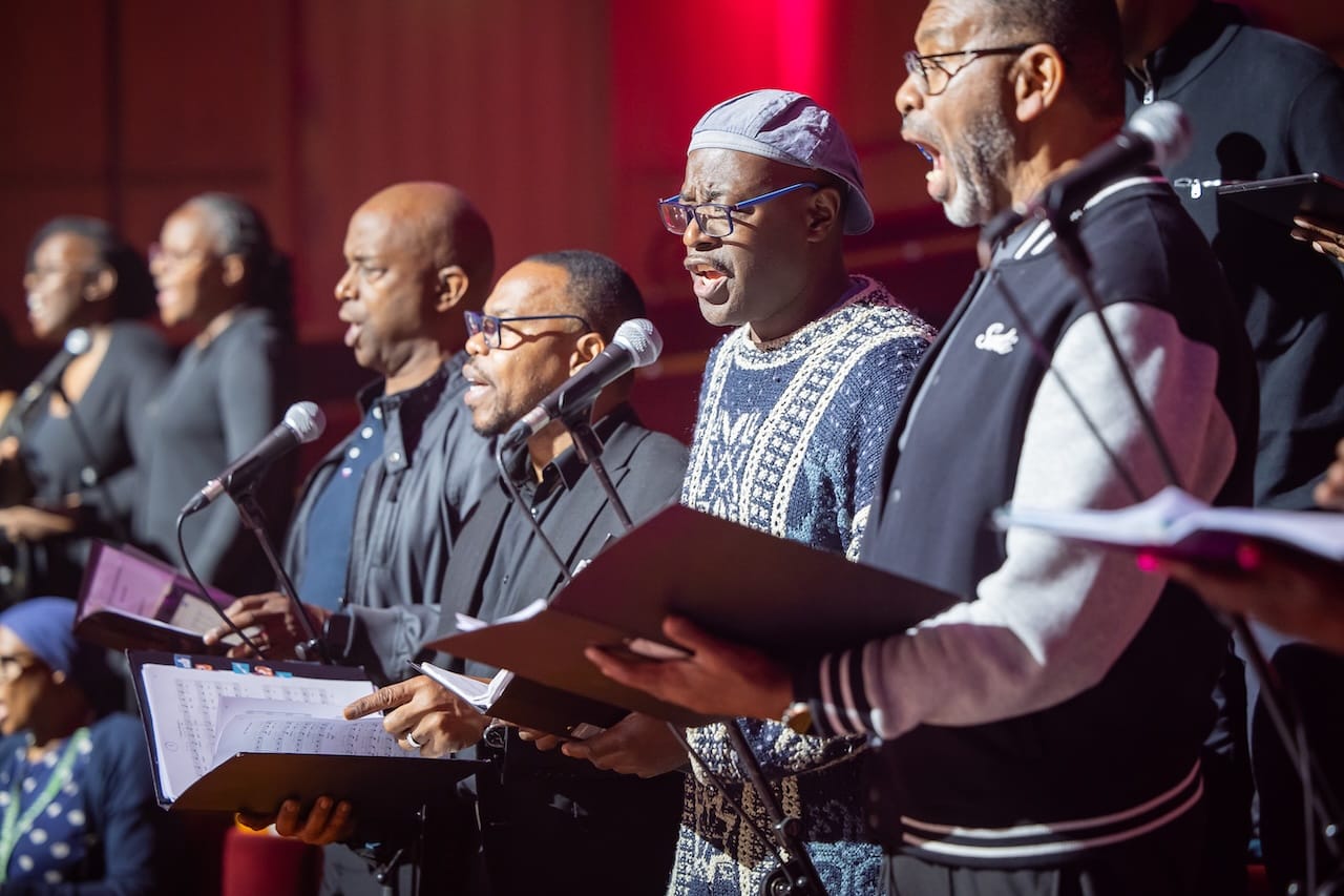 Four gospel singers look out to the audience as they sing into microphones.