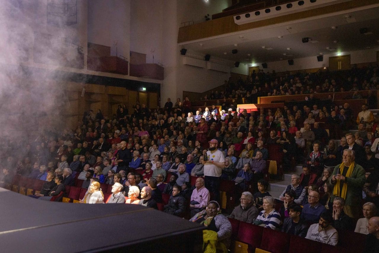 Darkened concert hall audience, with spotlight highlighting individuals.
