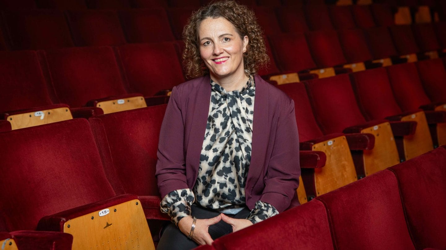 A smiling woman photographed in the red seats of a concert hall.