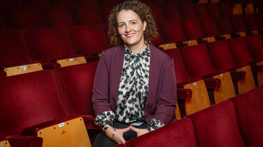 A smiling woman photographed in the red seats of a concert hall.