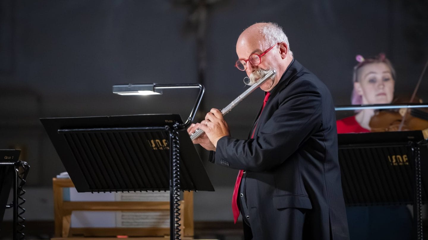 Man with red glasses and a moustache plays the flute.