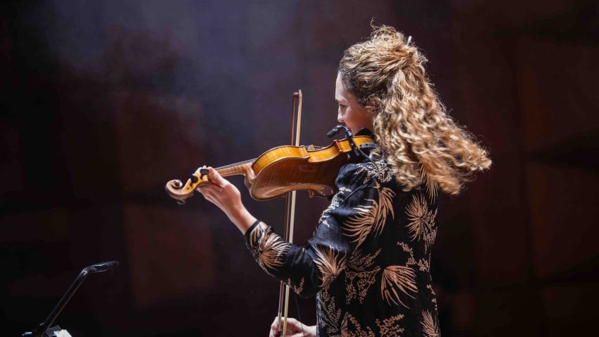 A woman stands playing the violin.