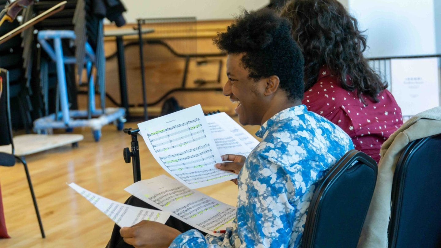 A man laughs while holding sheet music.