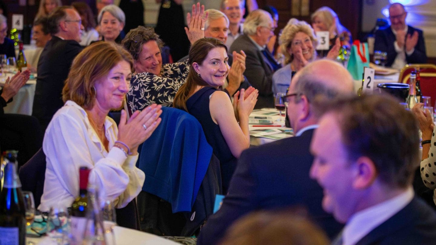Audience applaude sat around large tables.