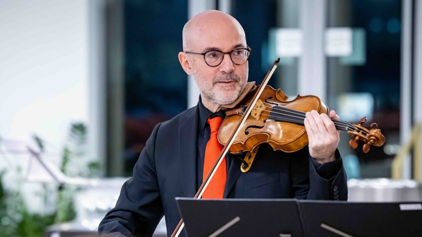 A man in black with red tie plays the violin.