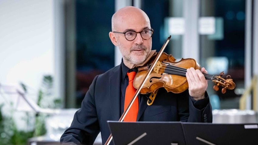 A man in black with red tie plays the violin.