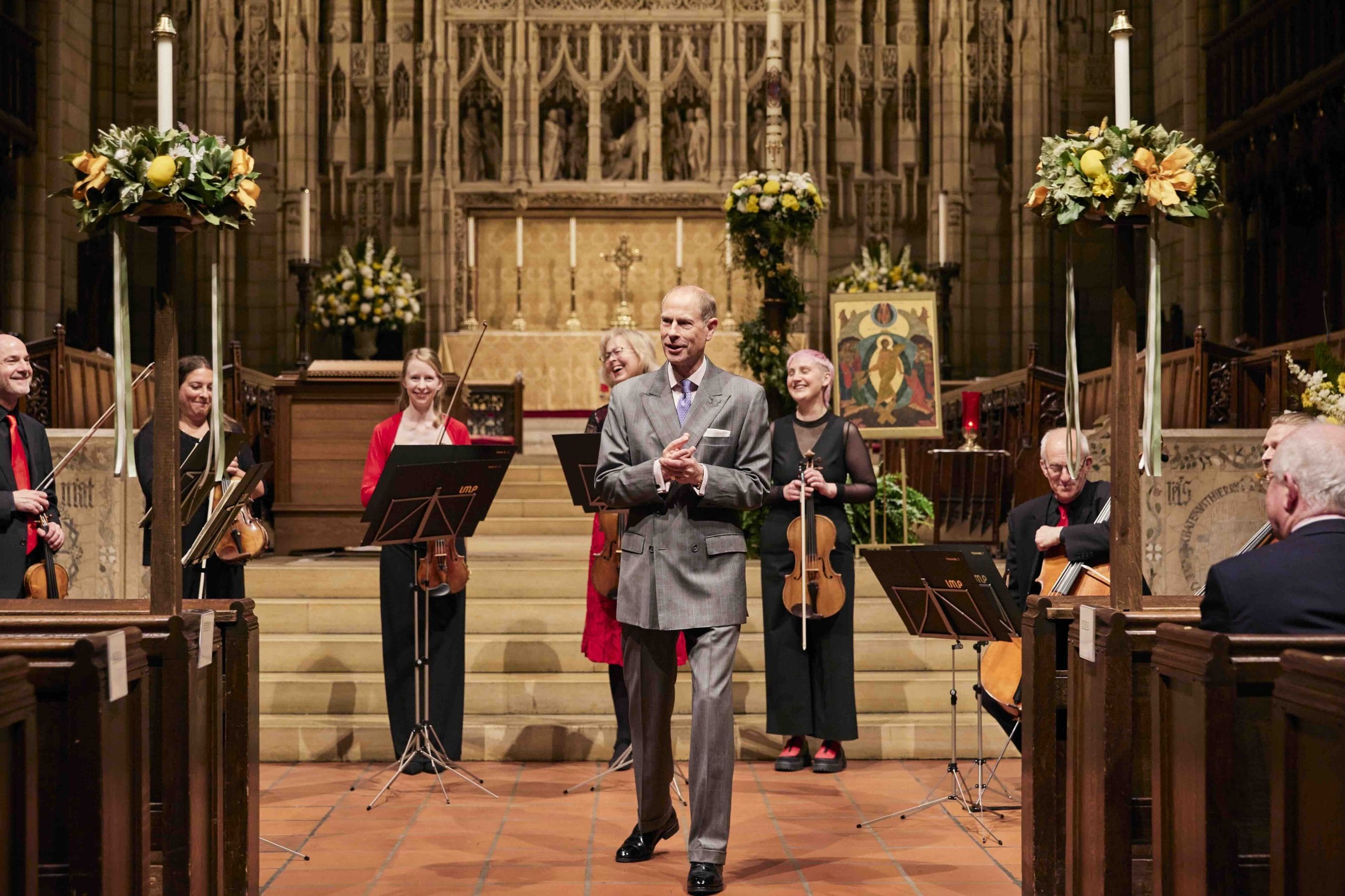 Prince Edward speaks with musicians stnading behind him with their instruments.