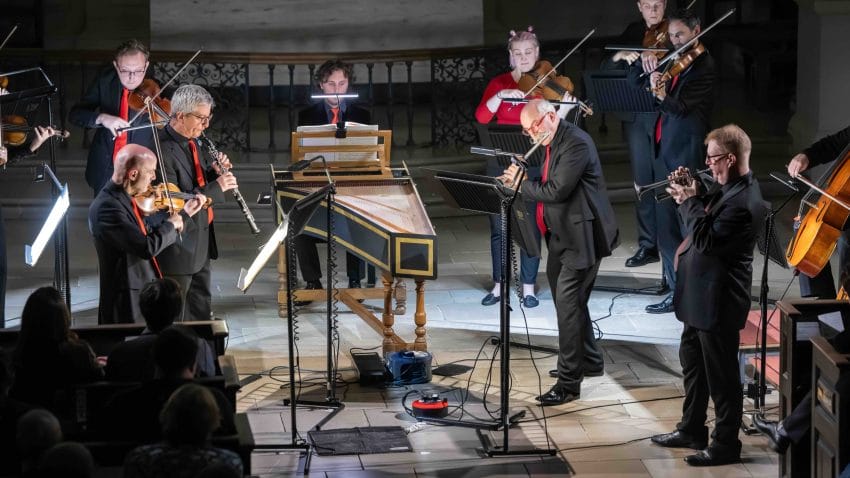 Musicians perform together around a harpsichord.