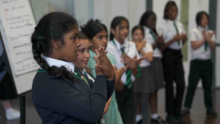 Child in school uniform mimes a butterfly with her hands.