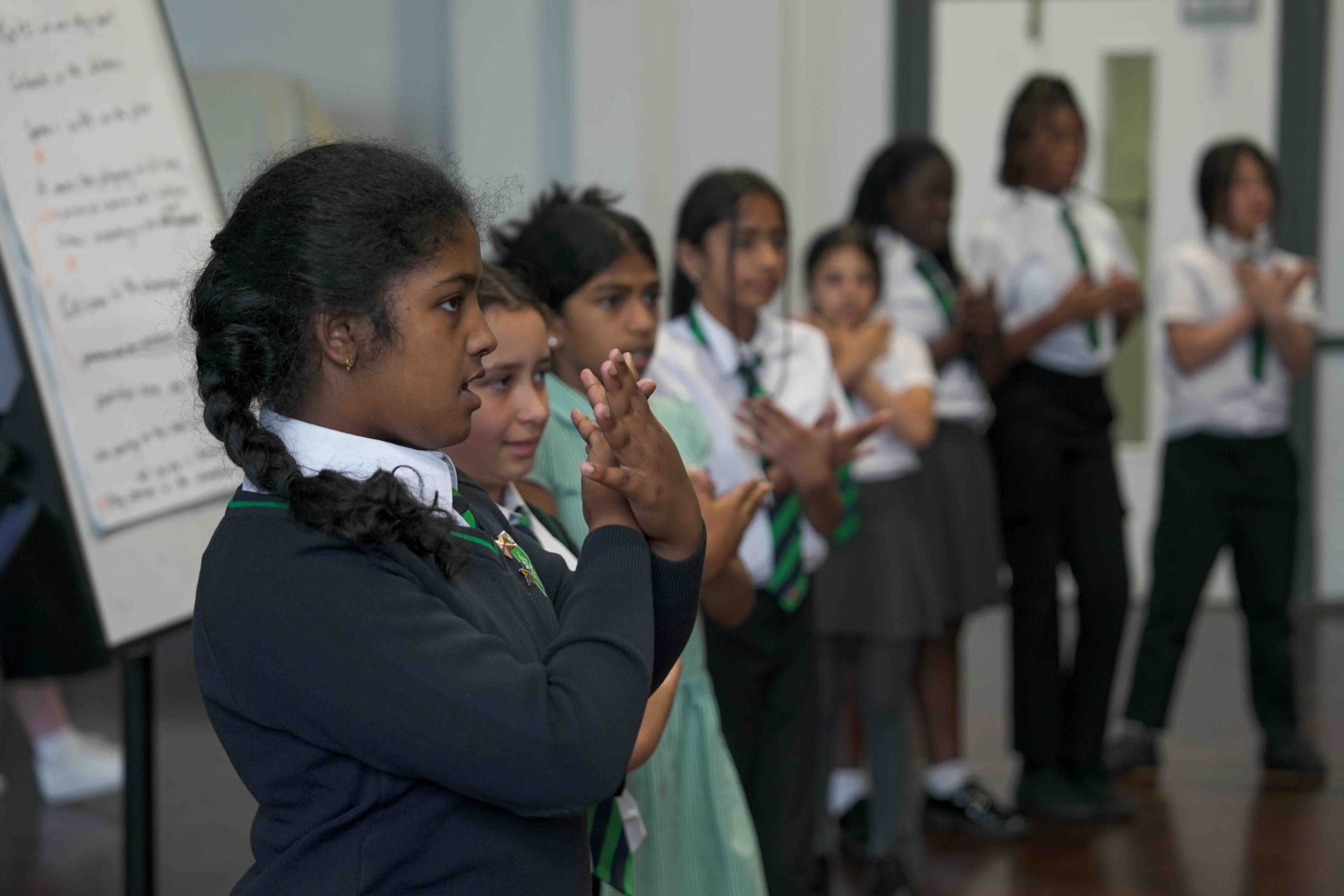 Child in school uniform mimes a butterfly with her hands.