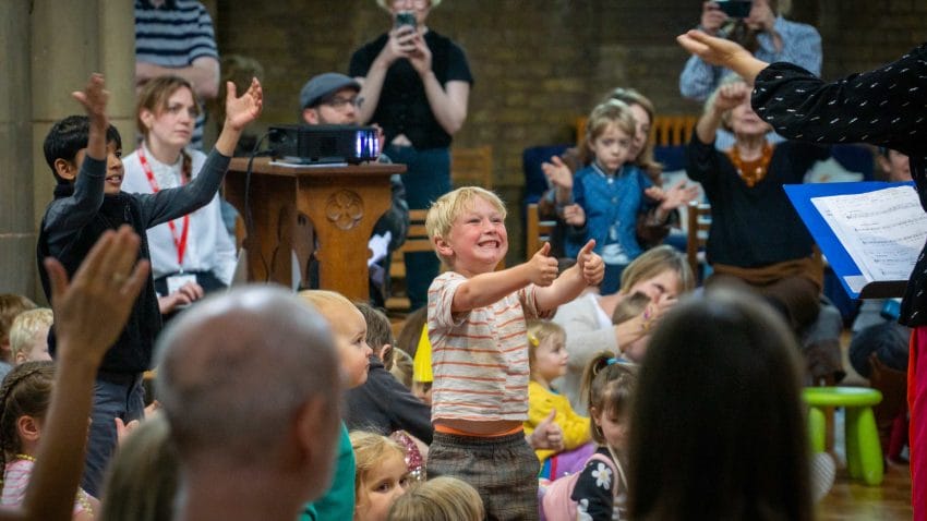 A young child stands in the audience and gives a double thumbs up.