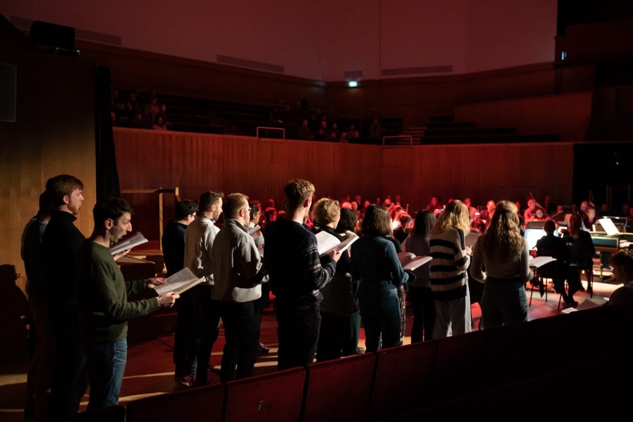 A group of singers stand behind one another.