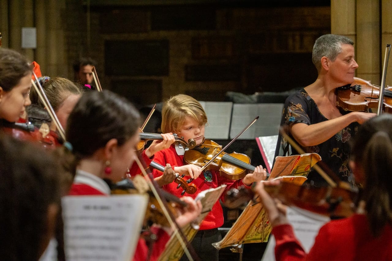 A young boy in a red school uniform plays the violin.