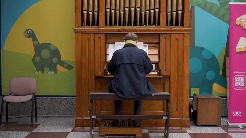 A man sits down on a bench playing a pipe organ.