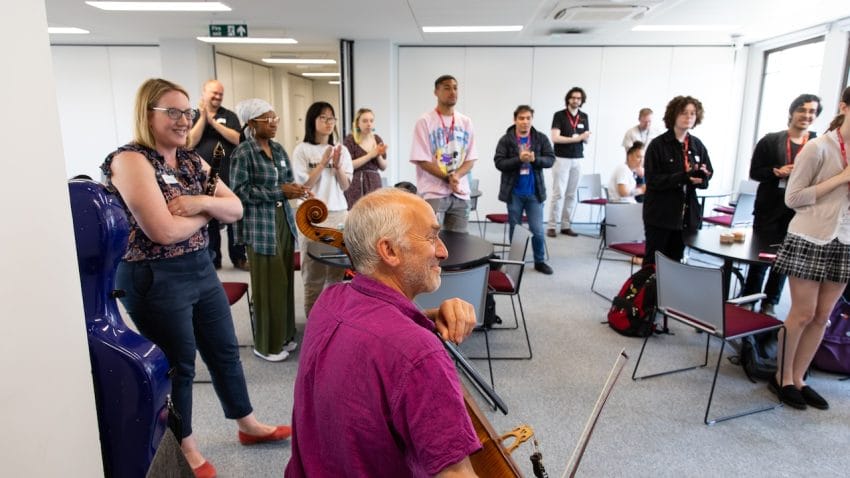 A group of students and a man holding a cello stand in a room together.