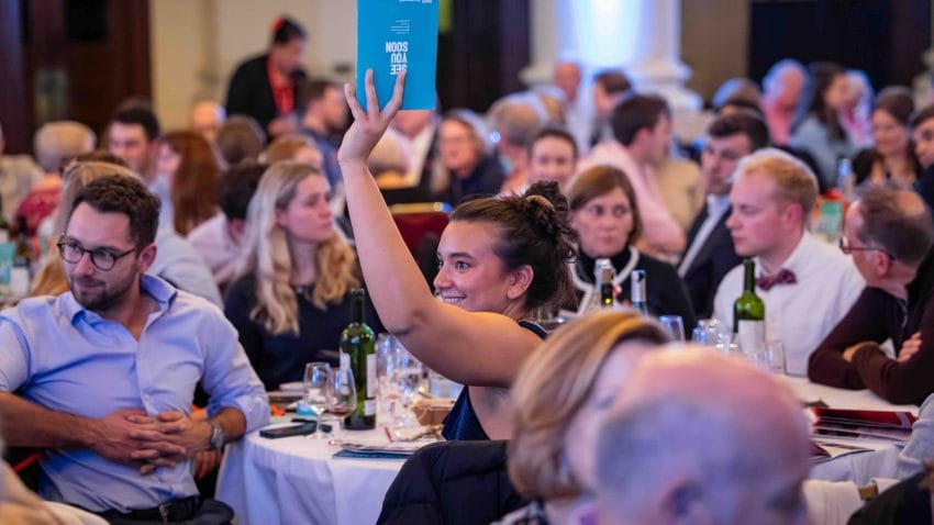 A woman holds up a blue programme at an auction.