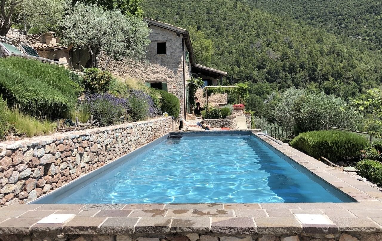 A beautiful, blue pool is drenched in sunlight amongst a backdrop of rolling Italian hills