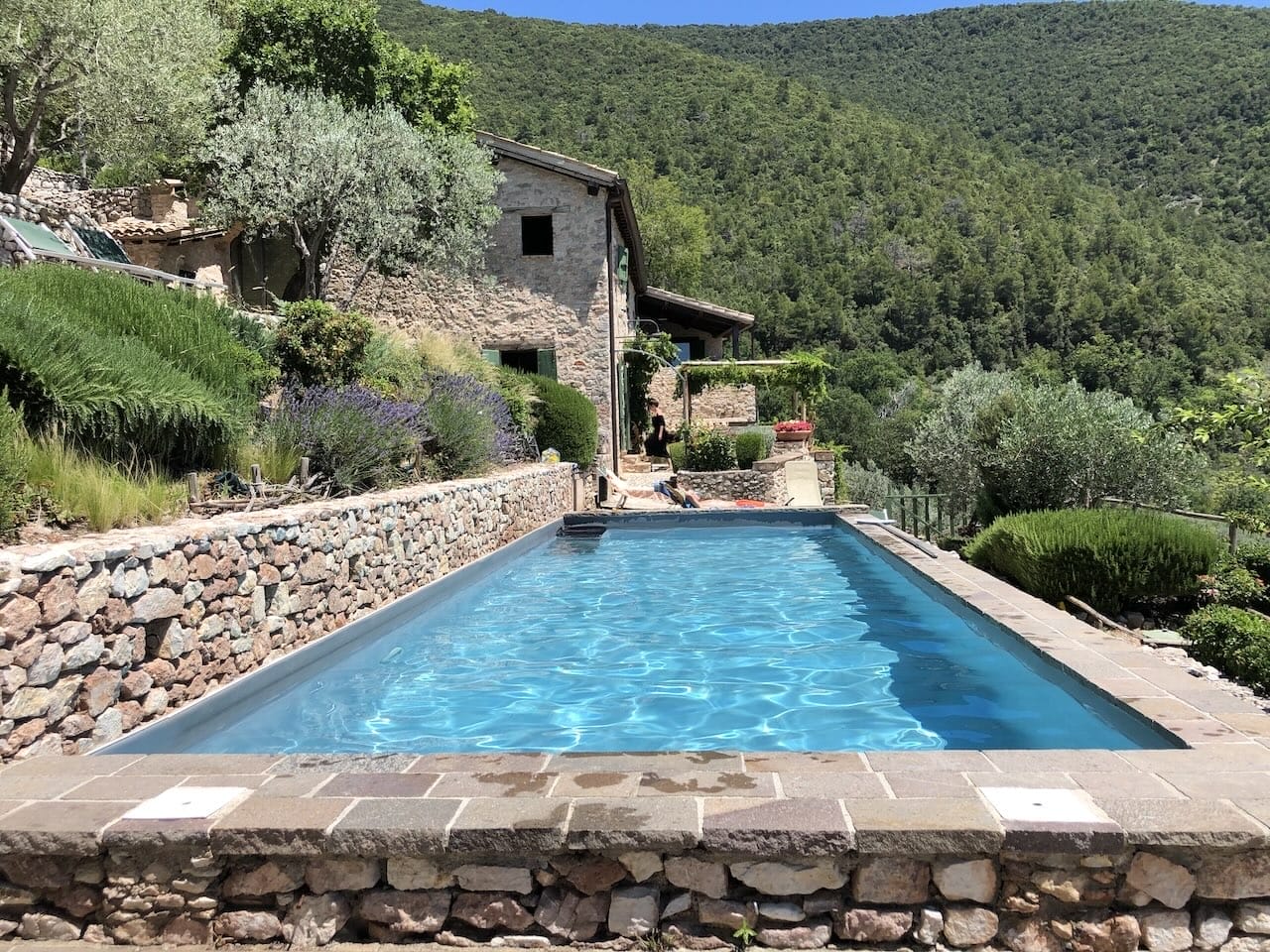 A beautiful, blue pool is drenched in sunlight amongst a backdrop of rolling Italian hills