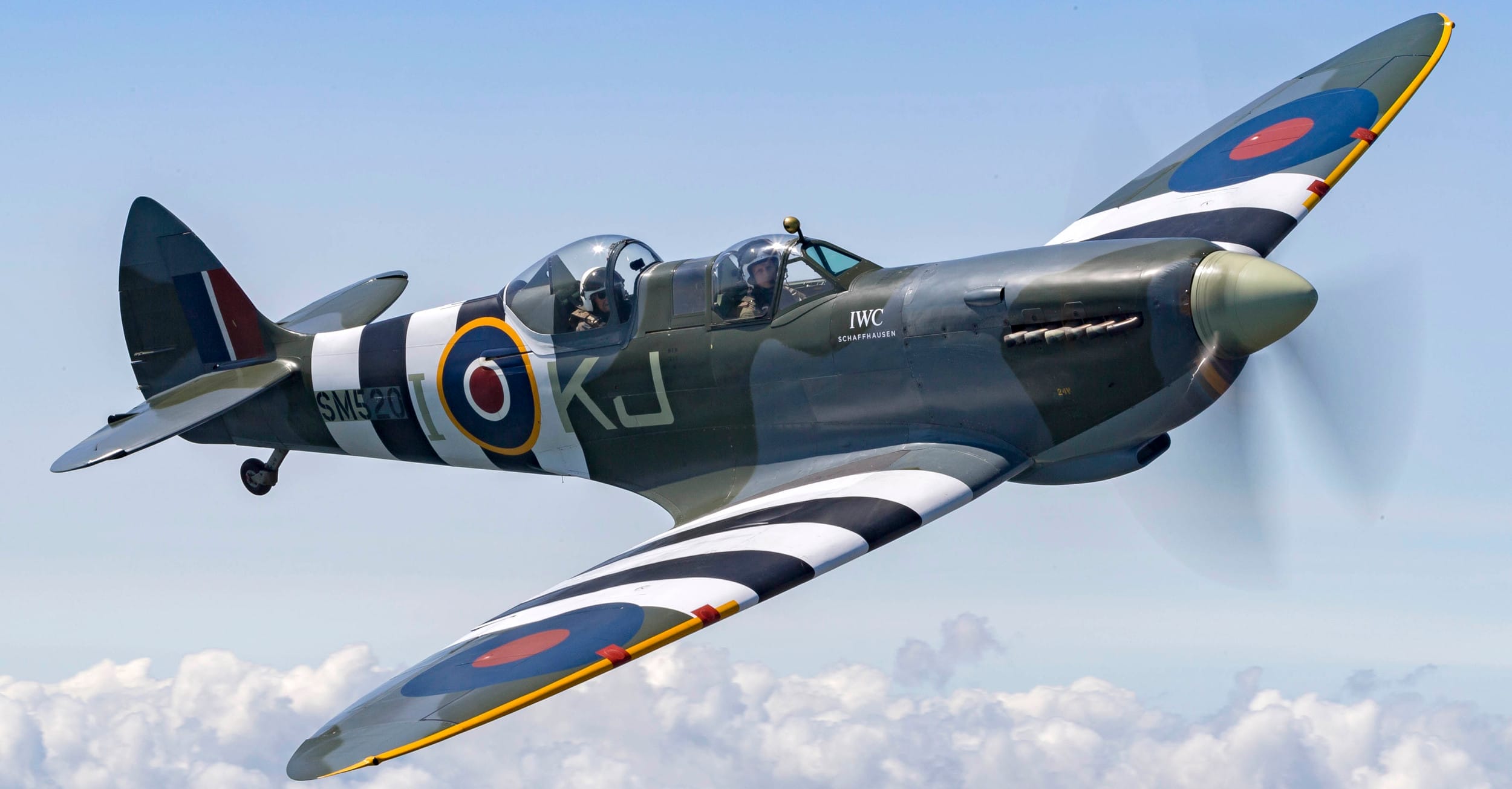 A spitfire in flight, soaring above white clouds.