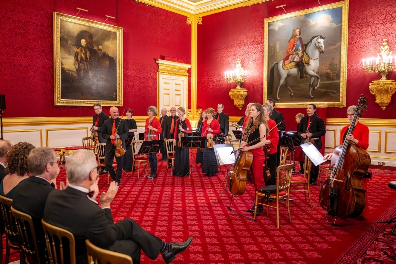 A group of players stand in an ornate, red room
